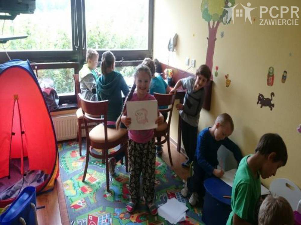 Zdjęcie: Dzieci uczestniczą w zajęciach plastycznych w sali, dziewczynka pokazuje swoją pracę